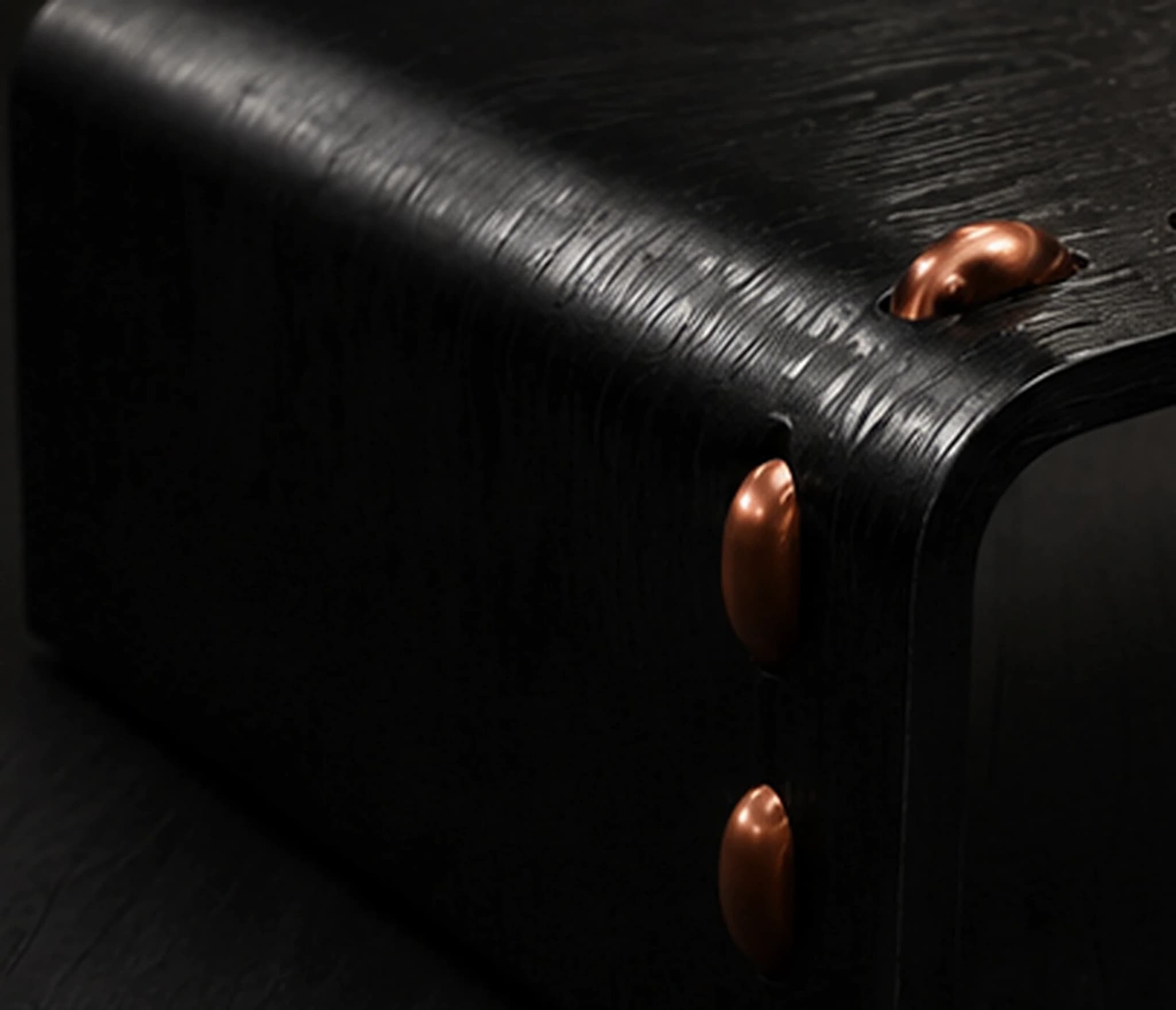 Close-up of the table's black leather grain wrapping the corner, with the thread studs following the edge