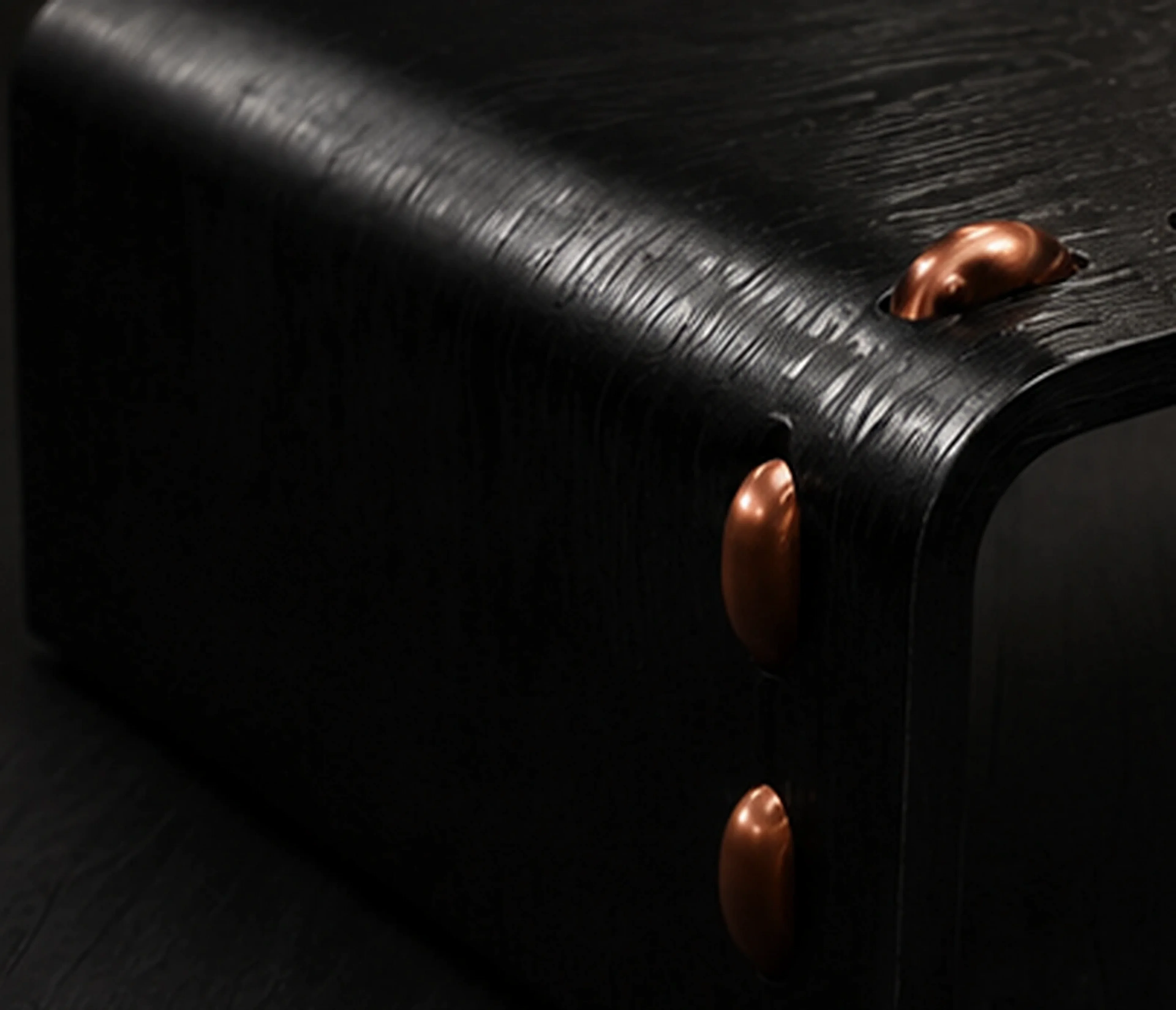 Close-up of the table's black leather grain wrapping the corner, with the thread studs following the edge